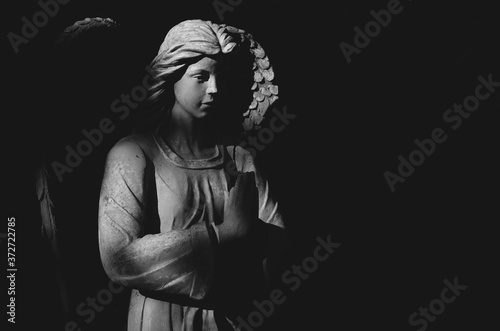 Angel statue praying in light and shadow. Black and white image.