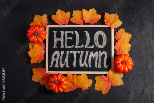 Hello autumn words text written on the backboard desk by the chalk with fall orange leaves and little pumpkins