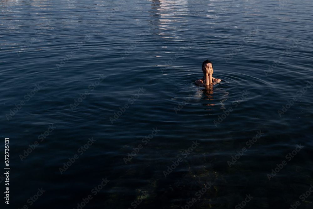 Fototapeta premium Young beautiful woman standing in the sea water.Young beautiful woman standing in the water and close her eyes with her hands.