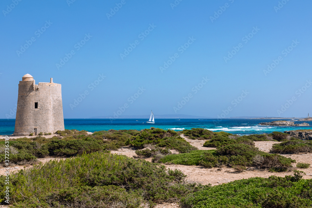 Beautiful view of the old observation tower (Torre De Ses Portes) and sailing yacht off the coast of Ibiza island