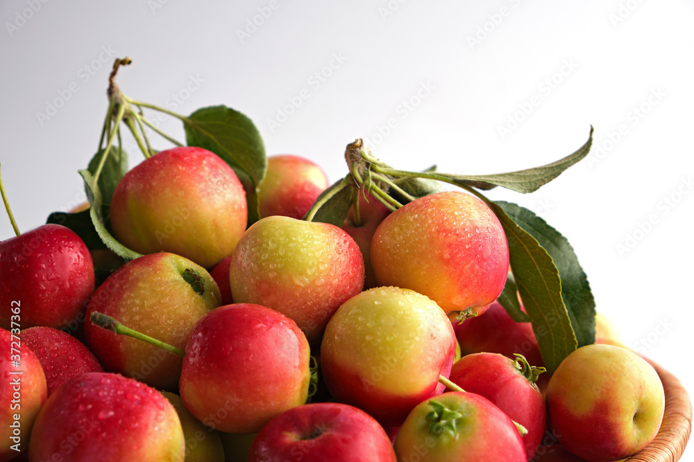 Red and yellow ripe apples with leaves close-up in a wicker basket on a light background. Close up. No people