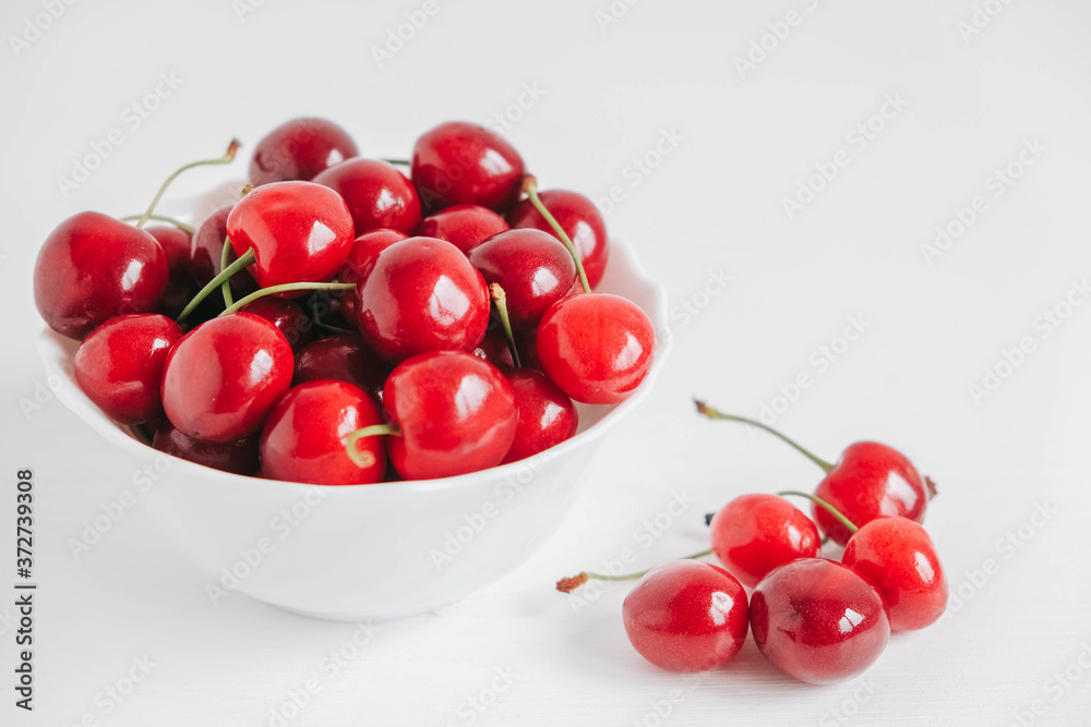 Fresh juicy red cherries in a white plate on the white wooden background. Copy, empty space for text Fresh juicy red cherries in a white plate on the white wooden background. Copy, empty space for text
