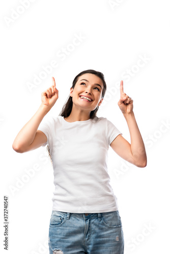 brunette woman in white t-shirt pointing with fingers and looking up isolated on white