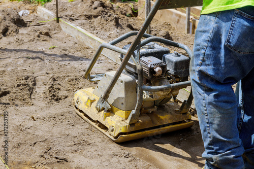 Worker uses compactor to vibratory hammer power tool at construction site