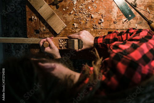 Mann mit Dreadlocks in rotem Hemd hobelt ein Stück Holz von oben aufgenommen