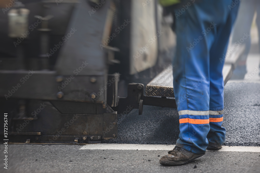 Asphalt paver machine and steam road roller during road construction and repairing works, process of asphalting and paving, workers working on the new road construction site, placing a layer