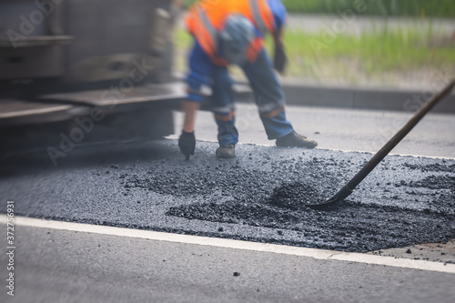 Asphalt paver machine and steam road roller during road construction and repairing works, process of asphalting and paving, workers working on the new road construction site, placing a layer