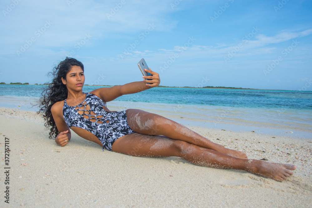 Young Brunette woman with blue swimwear and phone taking a selfie on sand Caribbean beach Young Brunette woman with blue swimwear and phone taking a selfie on sand Caribbean beach