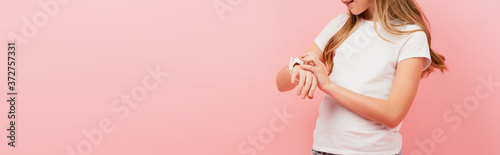 partial view of child in white t-shirt touching smartwatch isolated on pink, panoramic concept