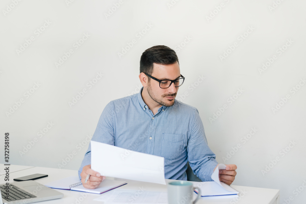 Portrait of serious young thoughtful confident businessman entrepreneur checking working plan and schedule or timetable in bright modern office copy space looking into data report information news