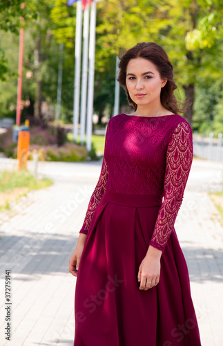 girl in a beautiful long burgundy dress in the summer on a city street