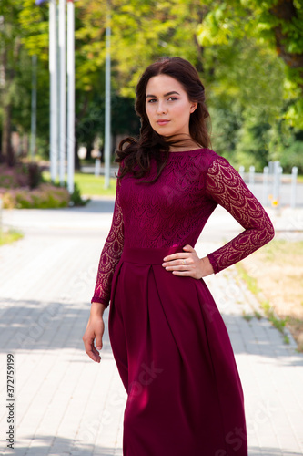 girl in a beautiful long burgundy dress in the summer on a city street © Inga