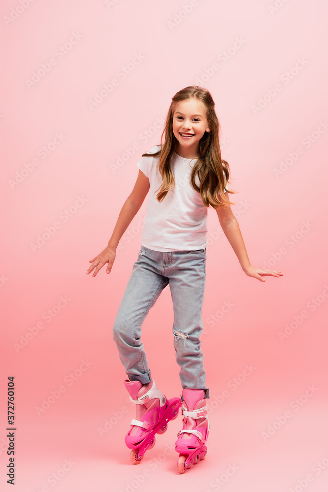 excited girl in white t-shirt, jeans and rolling skates looking at camera on pink excited girl in white t-shirt, jeans and rolling skates looking at camera on pink
