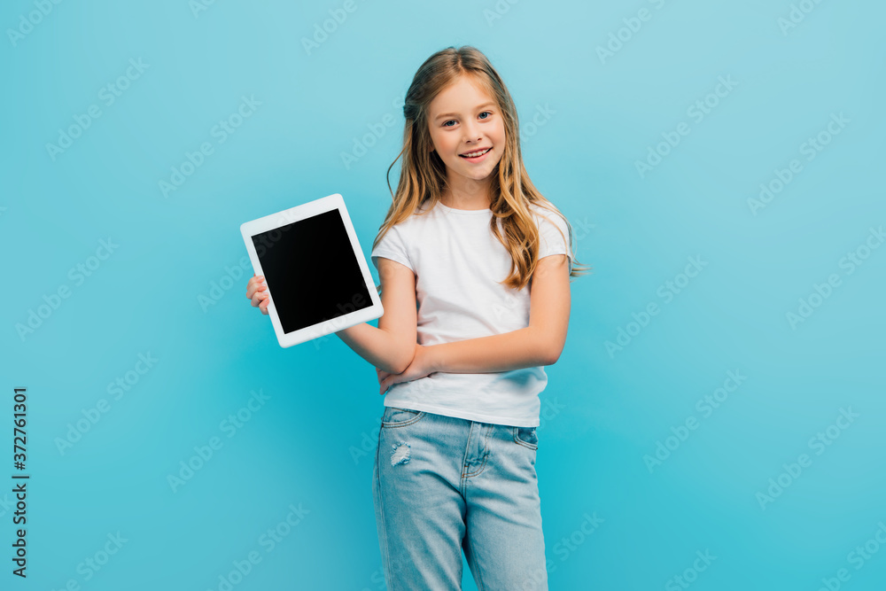 child in white t-shirt and jeans showing digital tablet while looking at camera isolated on blue child in white t-shirt and jeans showing digital tablet while looking at camera isolated on blue