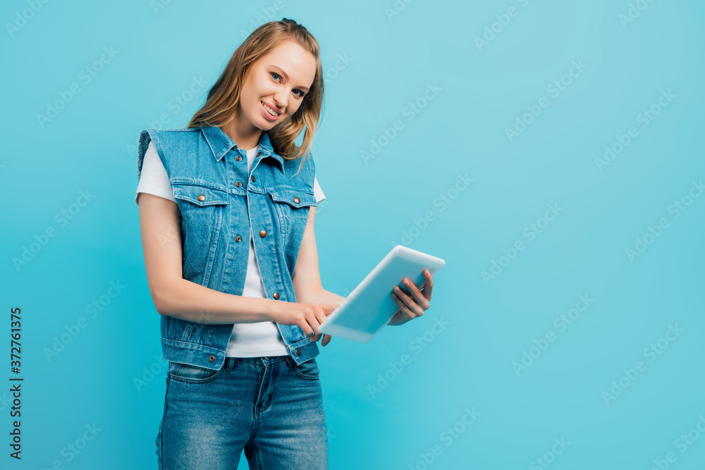 young woman in denim clothes using digital tablet while looking at camera isolated on blue young woman in denim clothes using digital tablet while looking at camera isolated on blue