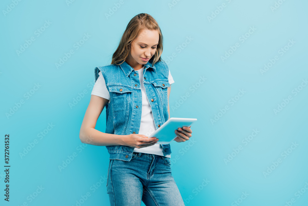 focused woman in denim clothes using digital tablet isolated on blue focused woman in denim clothes using digital tablet isolated on blue