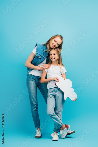 full length view of young woman in denim clothes touching daughter holding thought bubble on blue