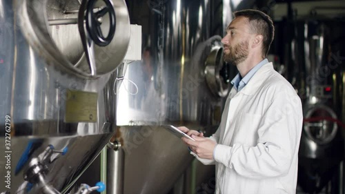 A joyful middle-aged labouring man in a white robe comparing readings with the help of his tablet. A side view slow motion close up
