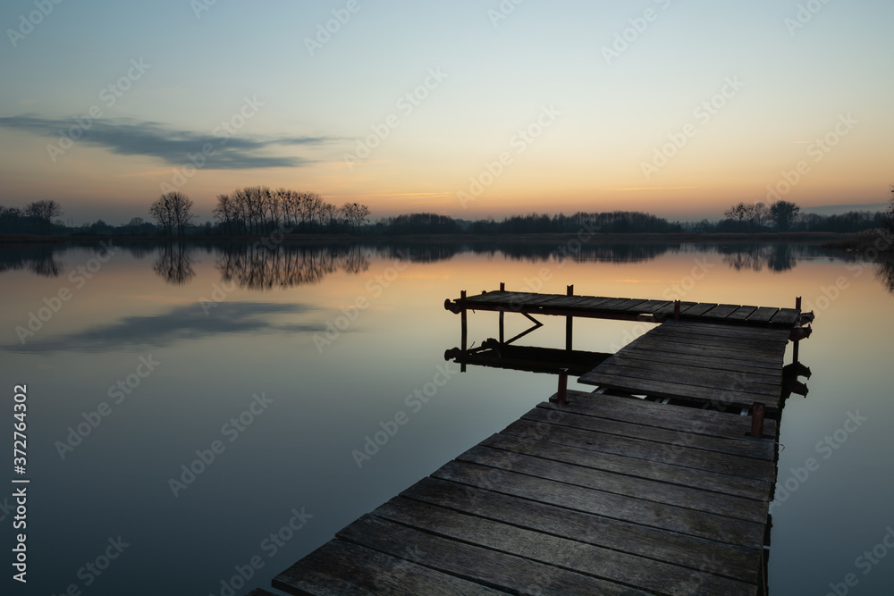 Wooden fishing platform on a calm lake and reflection of clouds in the water