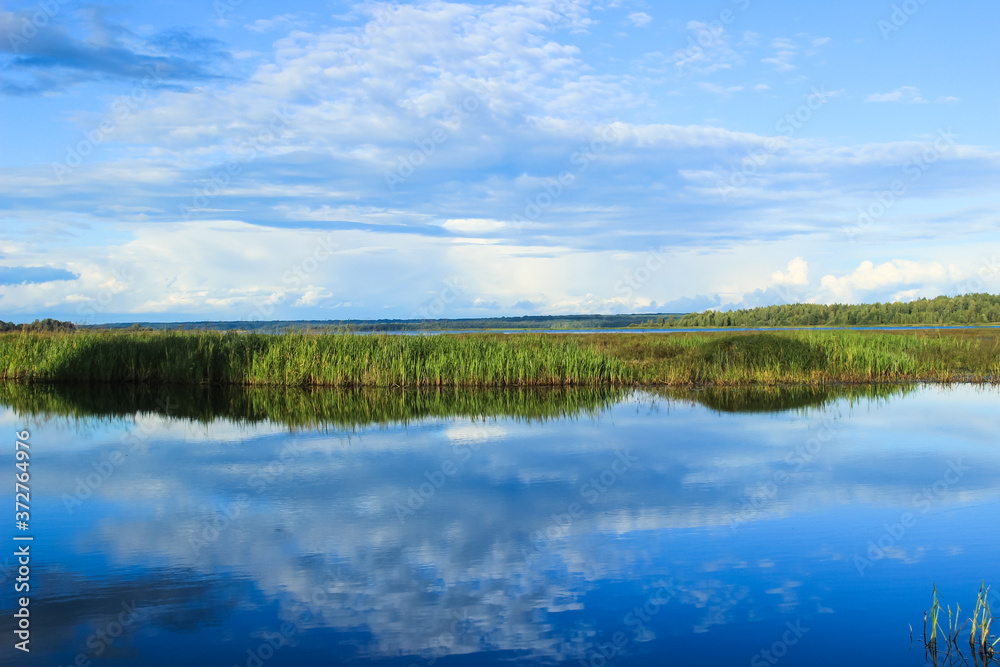 Beautiful blue sky in calm summer weather is reflected in the surface of the lake water. Countryside nature landscape.