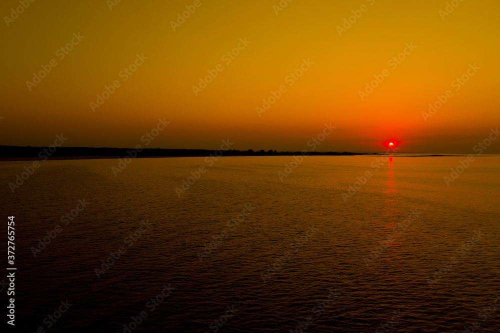 Naklejka premium Aerial photo from flying drone of a fascinating nature landscape with dramatic evening sunset sky which reflected in sea water with calm waves. Beautiful scenery of a Indian Ocean with sunrise