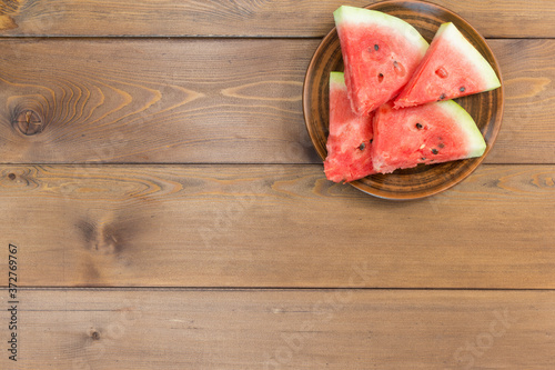 Four slices of ripe fresh watermelon on a plate on a brown wooden table. The view from the top