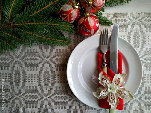 Christmas table setting. a knife and a fork laid out on a linen tablecloth wrapped in a red napkin on a white plate. 