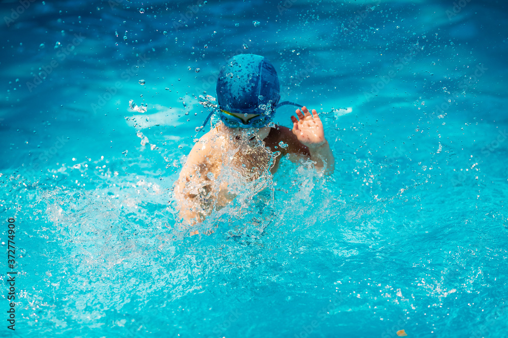 little boy in swimming glasses and a hat learns to swim in the pool