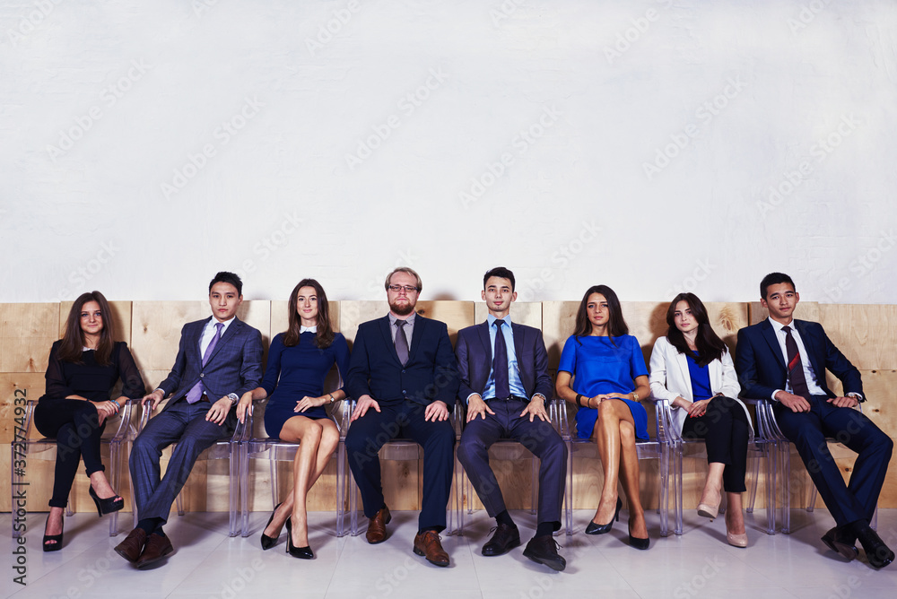 Fototapeta premium Full length portrait of successful professional financiers dressed in formal wear sitting in office hall before conference, multi ethnic group of prosperous workers waiting for start business meeting