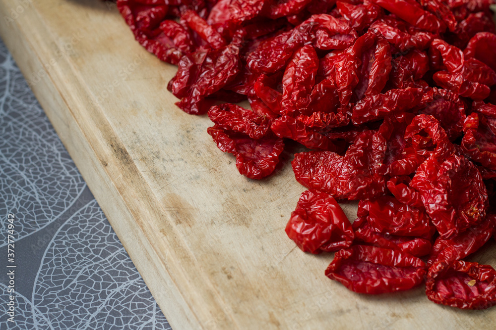 Close-up sun-dried tomatoes with spices and olive oil on wooden cutting board, background or concept, selective focus