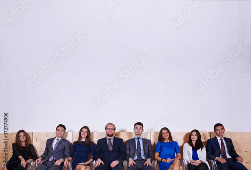 Portrait of a young confident workers dressed in corporate clothes sitting in hall before conference  multi ethnic group of successful entrepreneurs in formal wear waiting for start business meeting