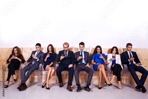 Full length portrait of a multi ethnic people dressed in corporate clothes using cell telephones while waiting for start interview  young intelligent lawyers chatting on smart phones during work break