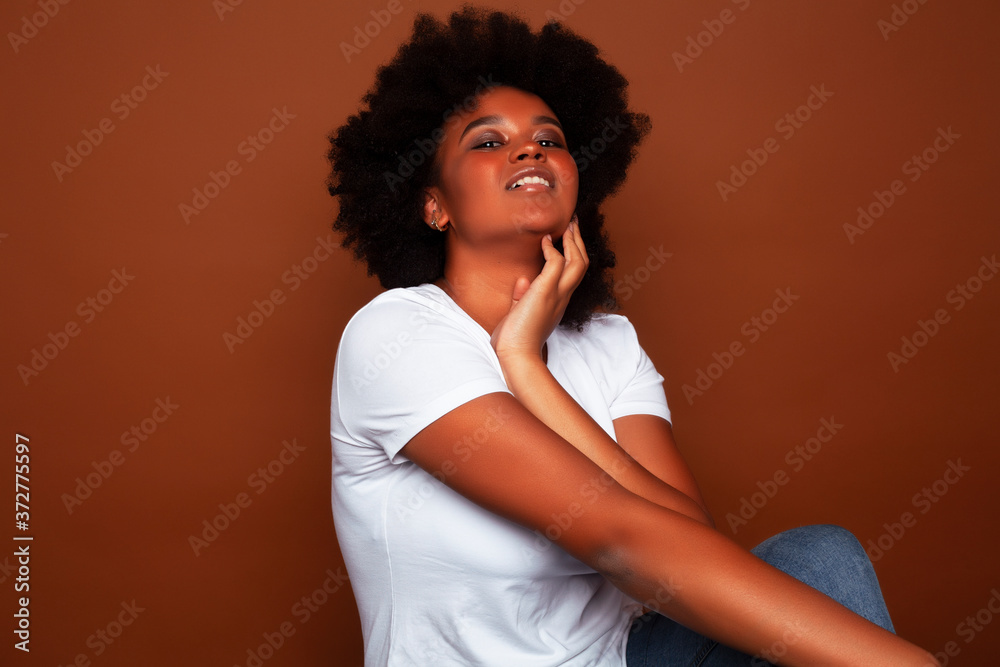 pretty young african american woman with curly hair posing cheerful gesturing on brown background, lifestyle people concept