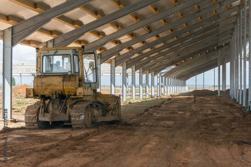 A bulldozer is leveling the ground in a barn under construction. Construction of an agricultural complex. Earthworks using special equipment. Bulldozer is pushing soil in a worksite A bulldozer is leveling the ground in a barn under construction. Construction of an agricultural complex. Earthworks using special equipment. Bulldozer is pushing soil in a worksite