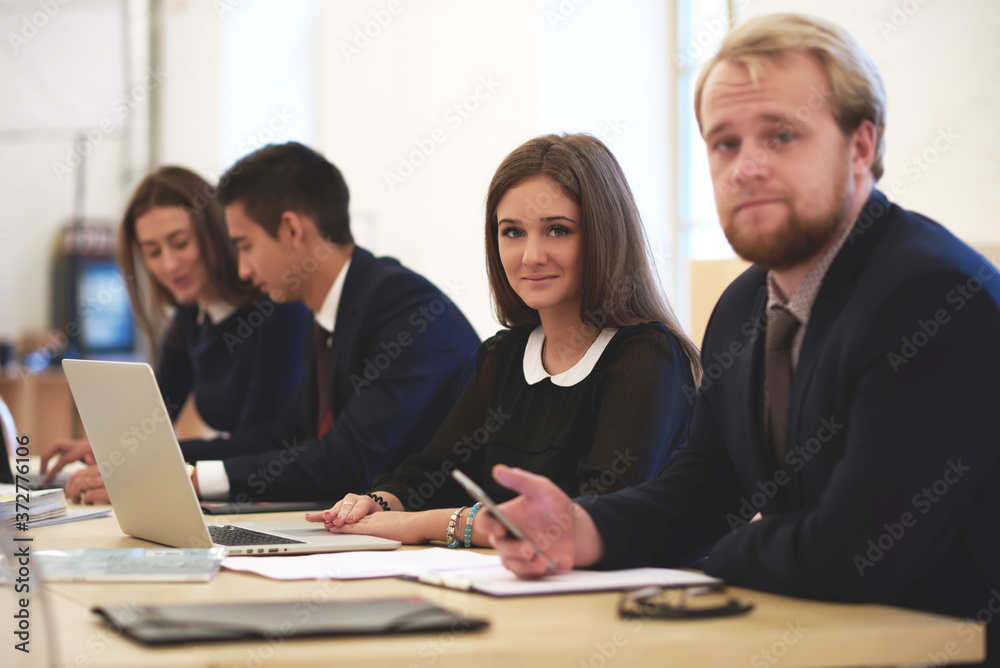 Young man and woman are using cell telephone and laptop computer during training in business school. Gorgeous female is taking break between work on net-book and posing for camera with her partner Young man and woman are using cell telephone and laptop computer during training in business school. Gorgeous female is taking break between work on net-book and posing for camera with her partner