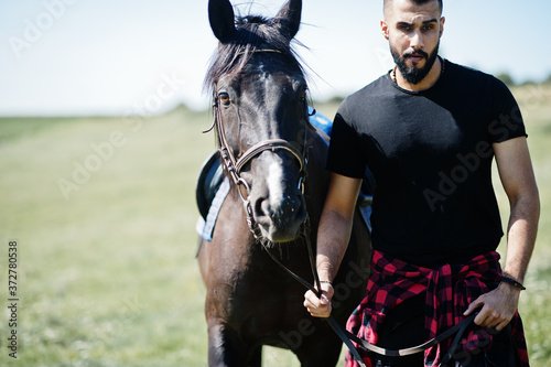 Arab tall beard man wear in black with arabian horse.