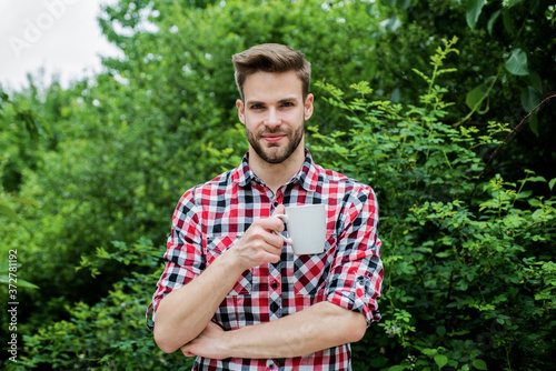 good morning. fresh inspiration and energetic beverage. handsome bearded guy drinking tea outdoor. he loves cocoa. food and drink. cheerful man in checkered shirt drink morning coffee