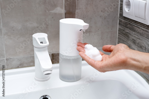 Obraz na płótnie A hand under the automatic soap dispenser with foam on a sink