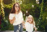 Family in a summer park. Mother in a blue pants. Little girl playing with bubbles.