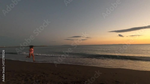 happy little girl running on the beach at sunset raising