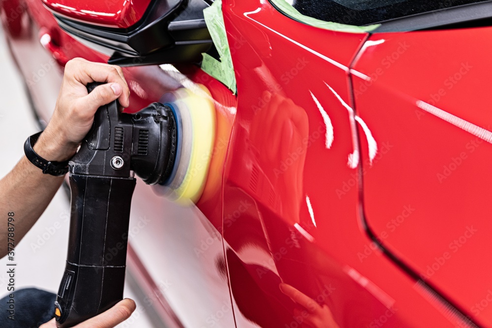 Man polishing car varnish with hand electric polisher.