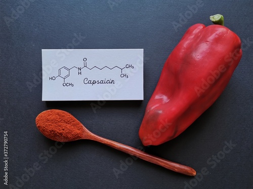 Structural chemical formula of capsaicin molecule with fresh red chili peppers and chili powder in wooden spoon. Capsaicin is the compound found in chili peppers that gives them their hot, spicy kick. photo