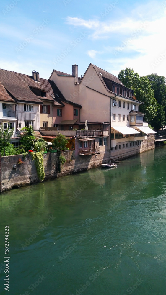 Obraz premium There are many residential houses on the banks of the river. Beautiful blue river, houses along the river, blue sky with clouds. Houses of residents of Switzerland. Travel to Switzerland. Europe.