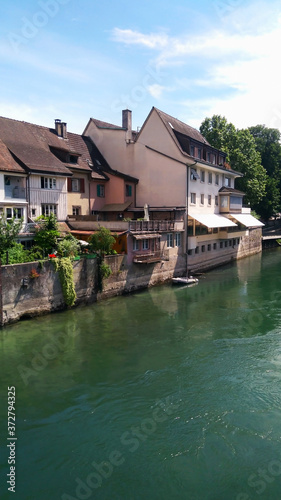 There are many residential houses on the banks of the river. Beautiful blue river, houses along the river, blue sky with clouds. Houses of residents of Switzerland. Travel to Switzerland. Europe.
