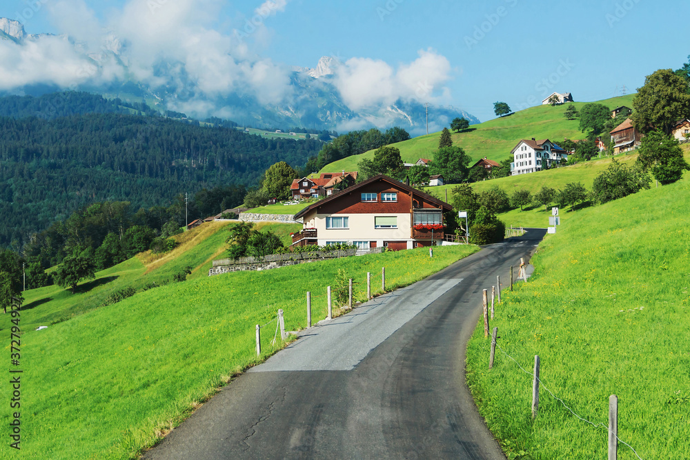 Small road in the mountains of Switzerland. Houses on the slopes of the Alps. Beautiful nature in the mountains. Tourism in Switzerland. Beautiful nature background. Clouds in the Alps.