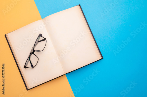 New eyeglasses and book on yellow and blue background. Copy space for text or design