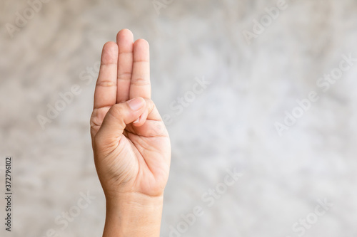 Hand showing three finger symbol on grey background with copy space © SKT Studio