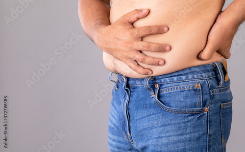Stomach ache or pain on belly concept : Man using his hand and pressing on stomach on grey