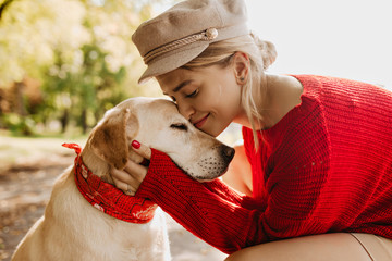 Closeup photo of pretty girl and her dog sitting in autumn the park. Lovely blonde having good time together with her pet.