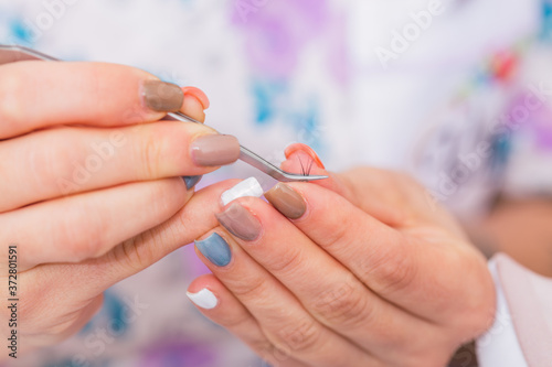 Woman s hand with false eyelashes on a tweezer.  Has painted nails. Concept of beauty and wellbeing.